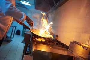 chef in hotel kitchen prepare vegetable food with fire